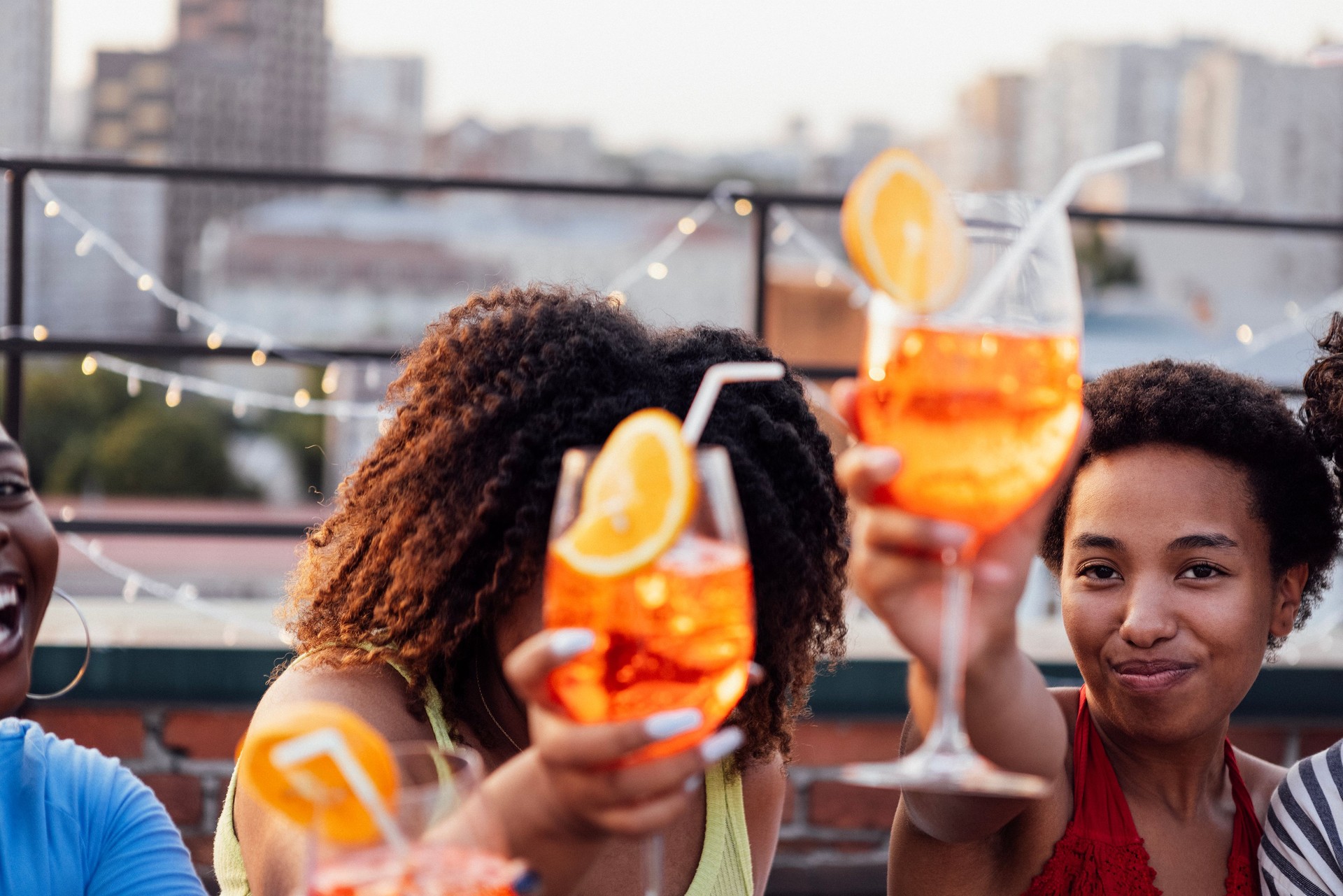 Company of four cheerful friends are enjoying tasty cocktails. Roof party