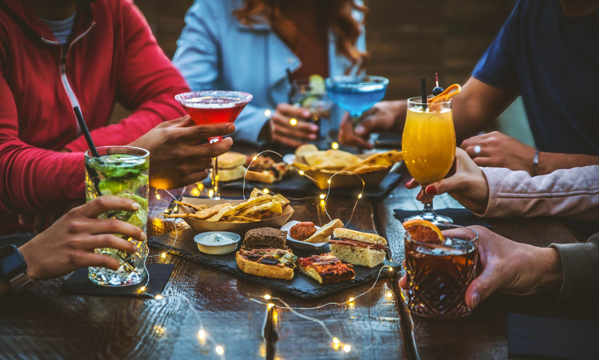 Group of people drinking alcohol and eating appetizers sitting at cocktail bar - Friends enjoying happy hour at brewery pub restaurant - Food and beverage life style concept