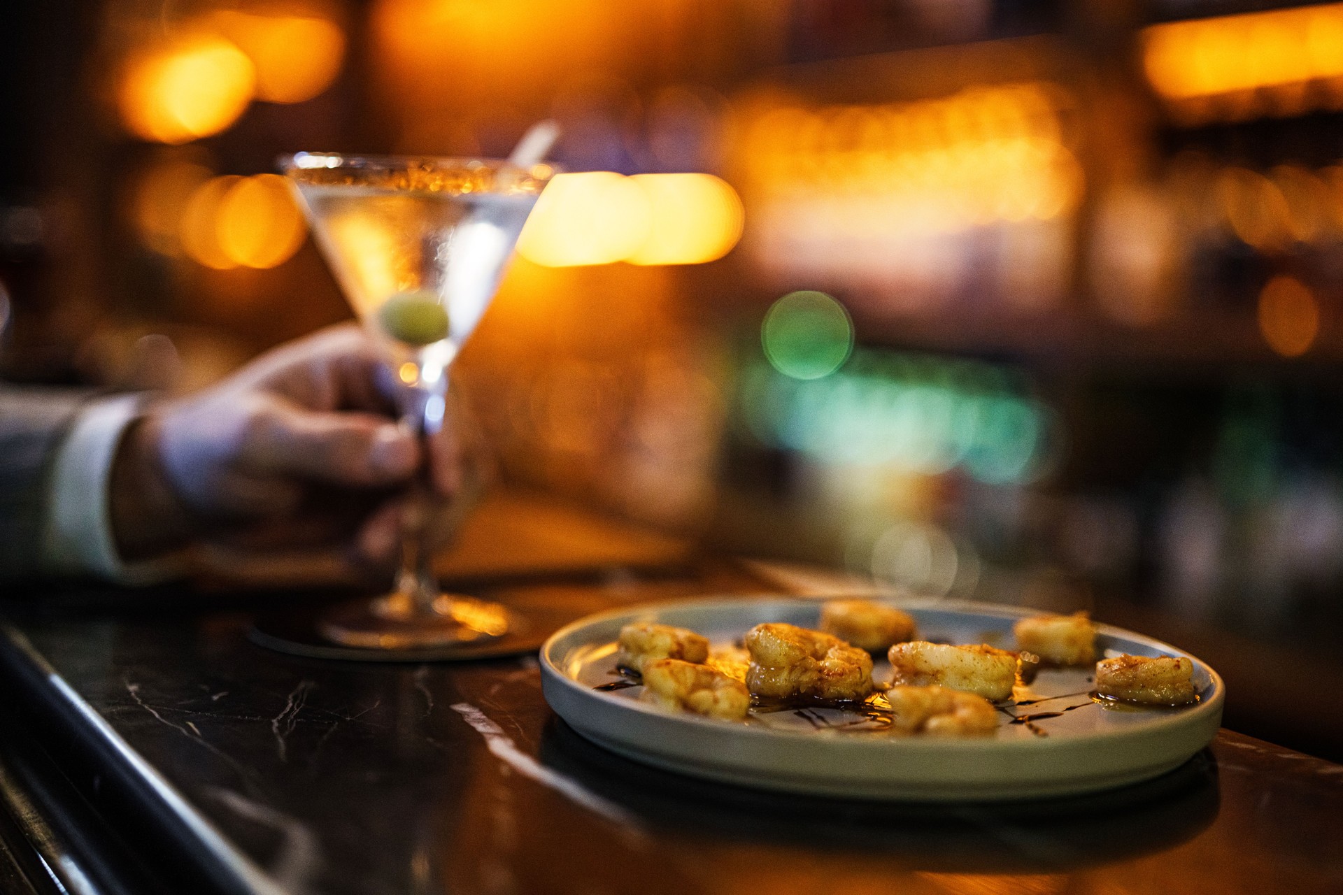 Close-up shot man's hand holding a dry martini next to shrimp tapas.